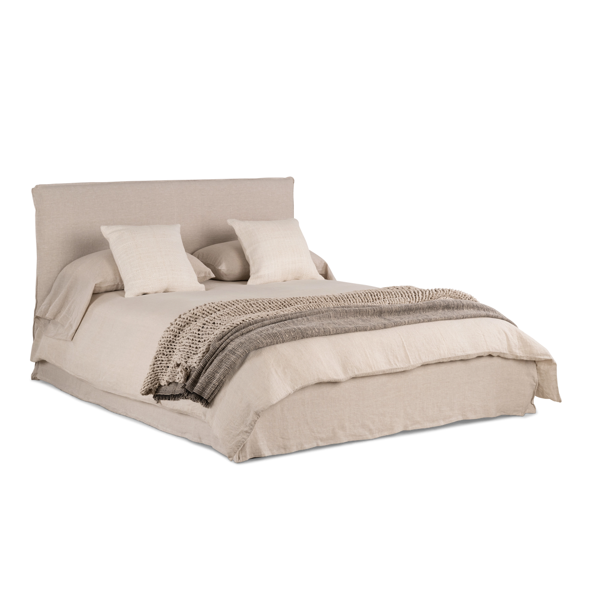 Muse Queen Bed in an angled view in natural linen, with a slipcovered headboard and floor-length skirt, styled with linen bedding, cushions and a throw.