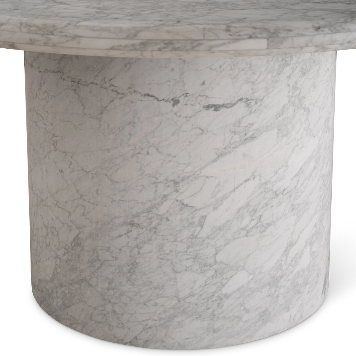 Aldo Dining Table detail view in white Arabescato marble, highlighting the cylindrical pedestal base, its flowing gray veining, and the rounded rim of the top above.