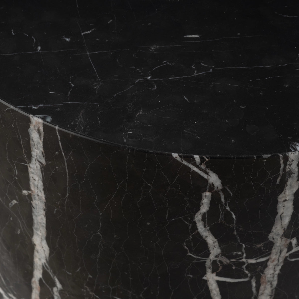 Close-up of the rim of the Meta Round Side Table in Black Nero Marquina marble, showing the clean edge where the honed top meets the curved side and a thick white vein with a faint blush tint.
