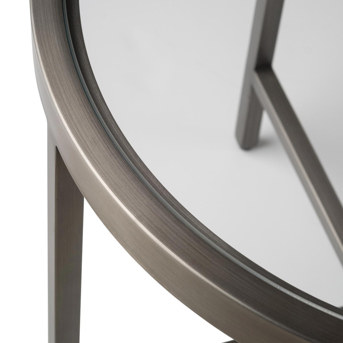Close-up showing the rim of the Tenor Side Table in Aged Pewter, with the fine brushed grain of the metal ring, the clear glass edge, and one leg meeting the underside of the frame.