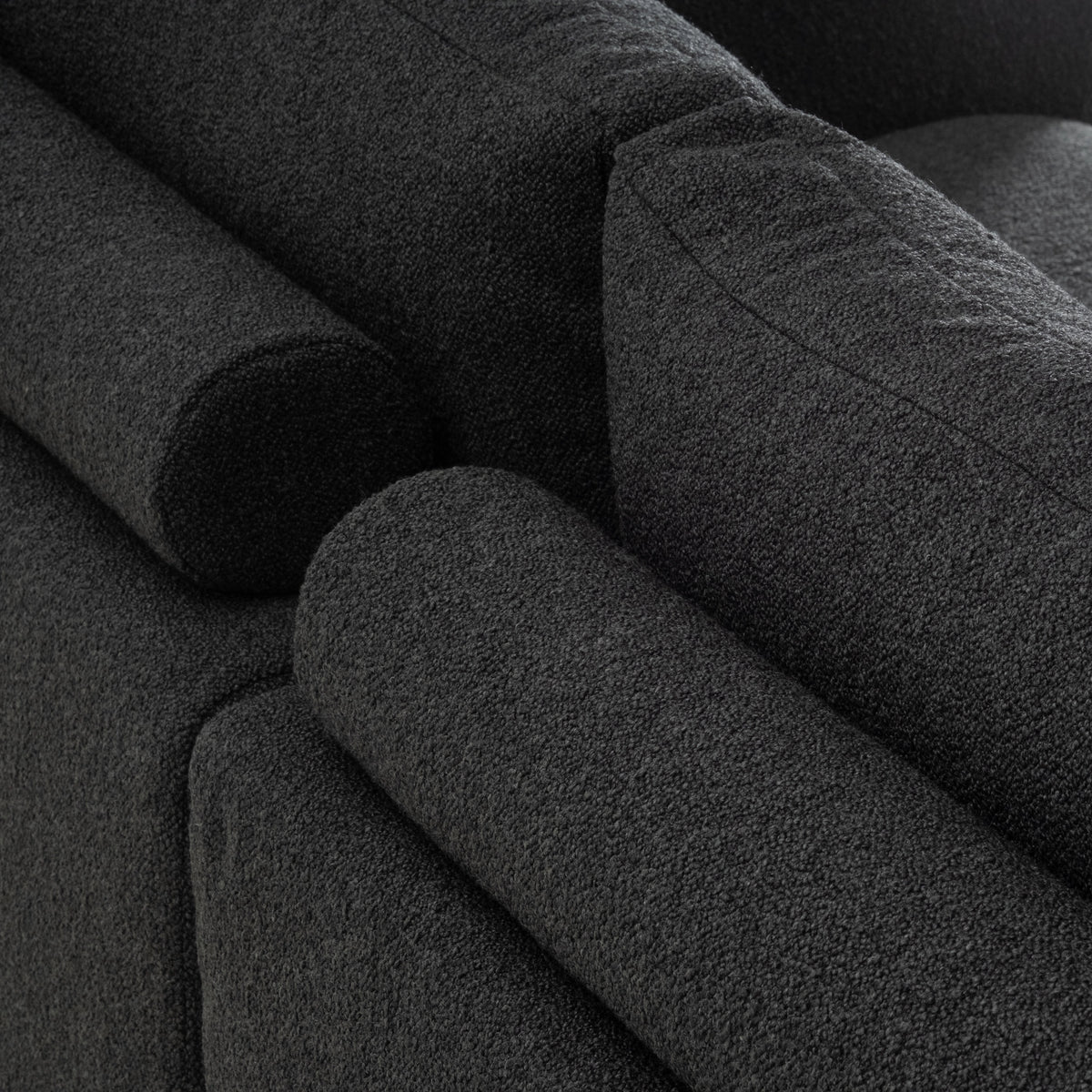 Close-up of the Colonna Modular Sectional in charcoal bouclé, showing the cylindrical bolster pillows and stitched back cushion edge in a dense, nubby weave.