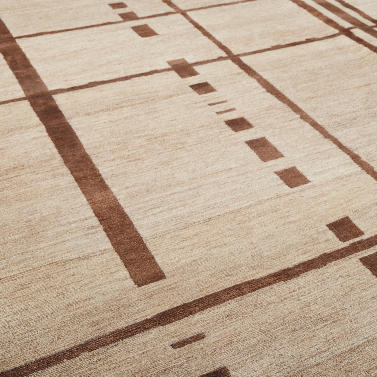A close-up of a textured area rug with a geometric pattern in warm brown on a light beige background.