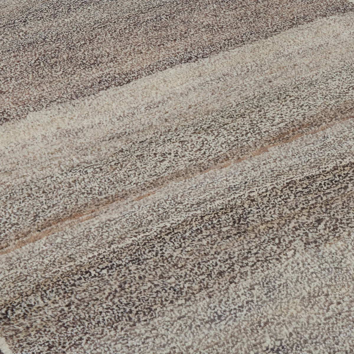A close-up of a textured area rug with a shaggy pile, featuring a diagonal striped pattern in shades of taupe, beige, brown, and gray.