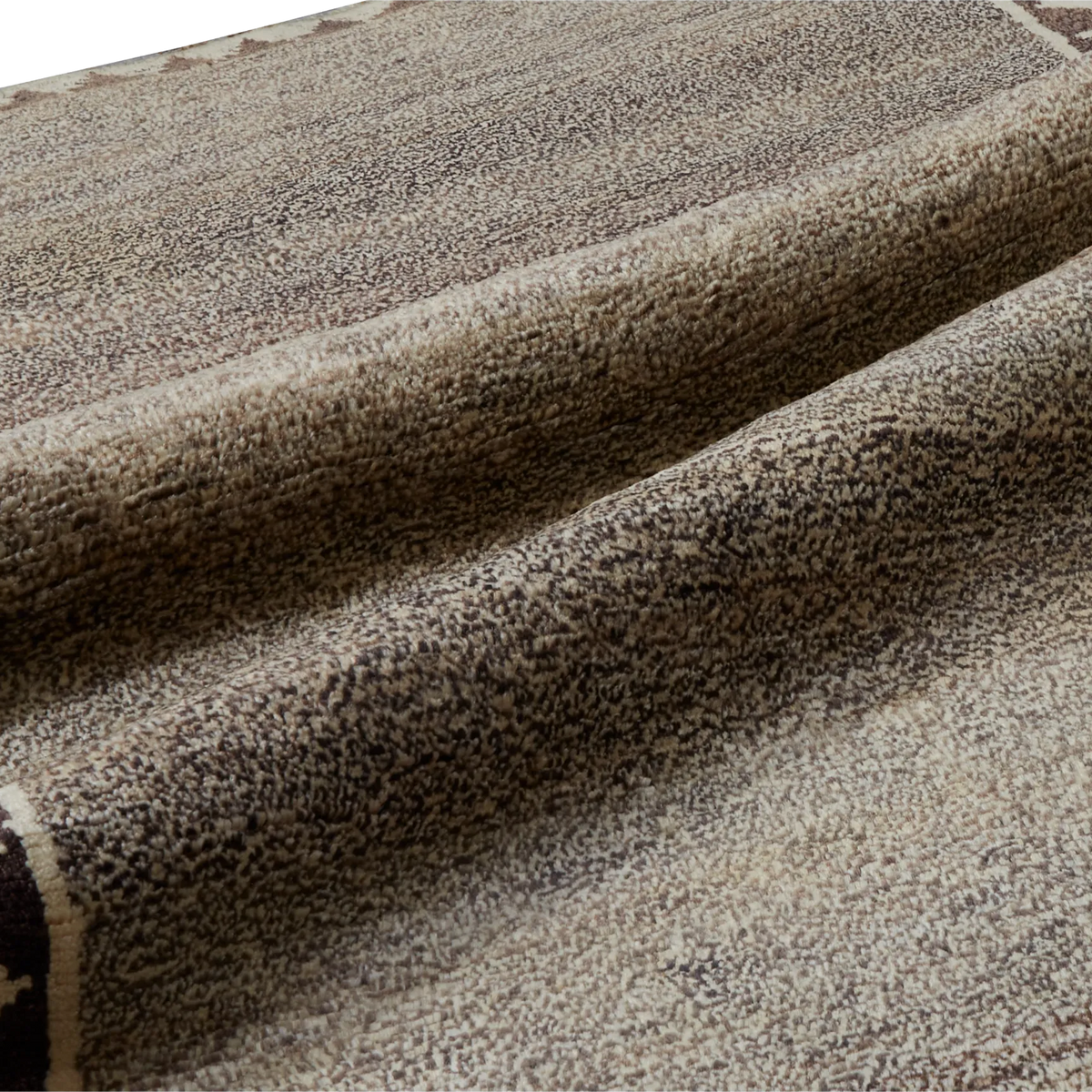 A close-up of a textured area rug with a mottled pattern of beige, brown, and gray fibers, draped to show its pile and texture.