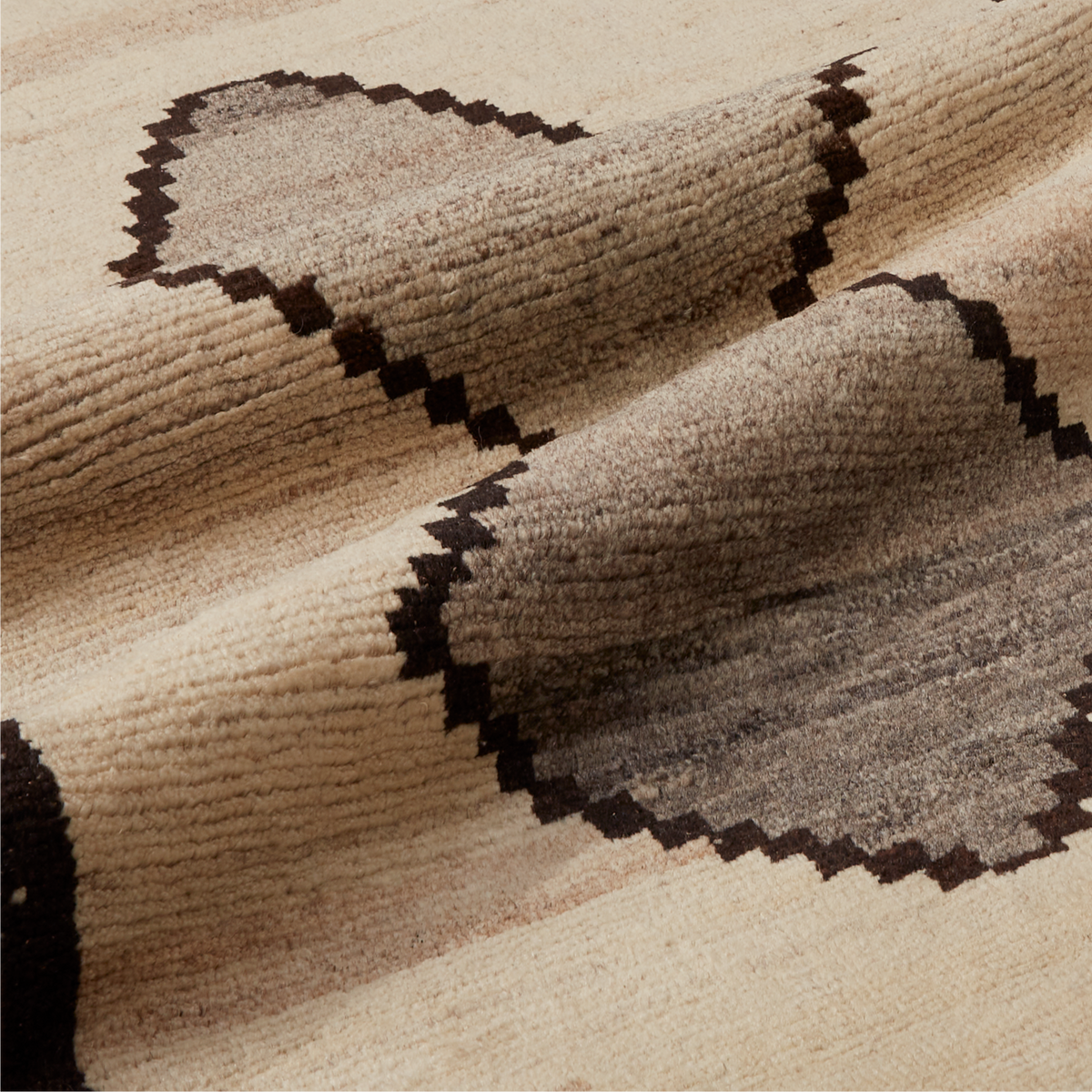 A close-up of a textured woven textile, likely a rug or blanket, featuring a pixelated geometric heart pattern in dark brown on a warm beige background.