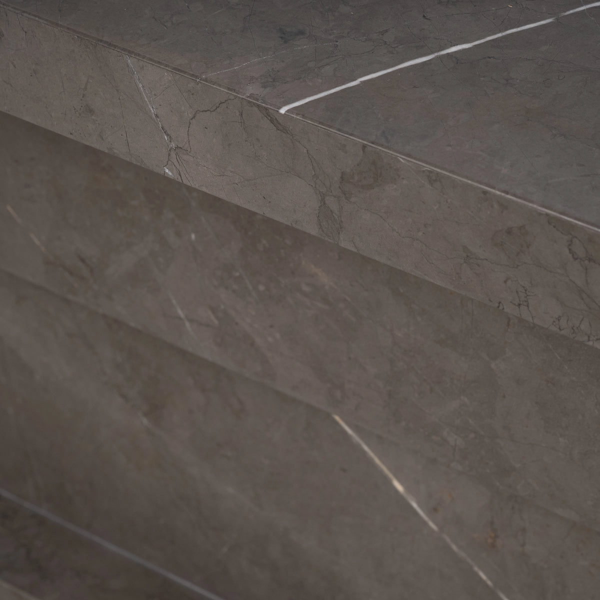 Balance Console Table close-up in warm gray Petra Grey marble, showing the edge of the top slab above a stacked block traced with fine white veining.