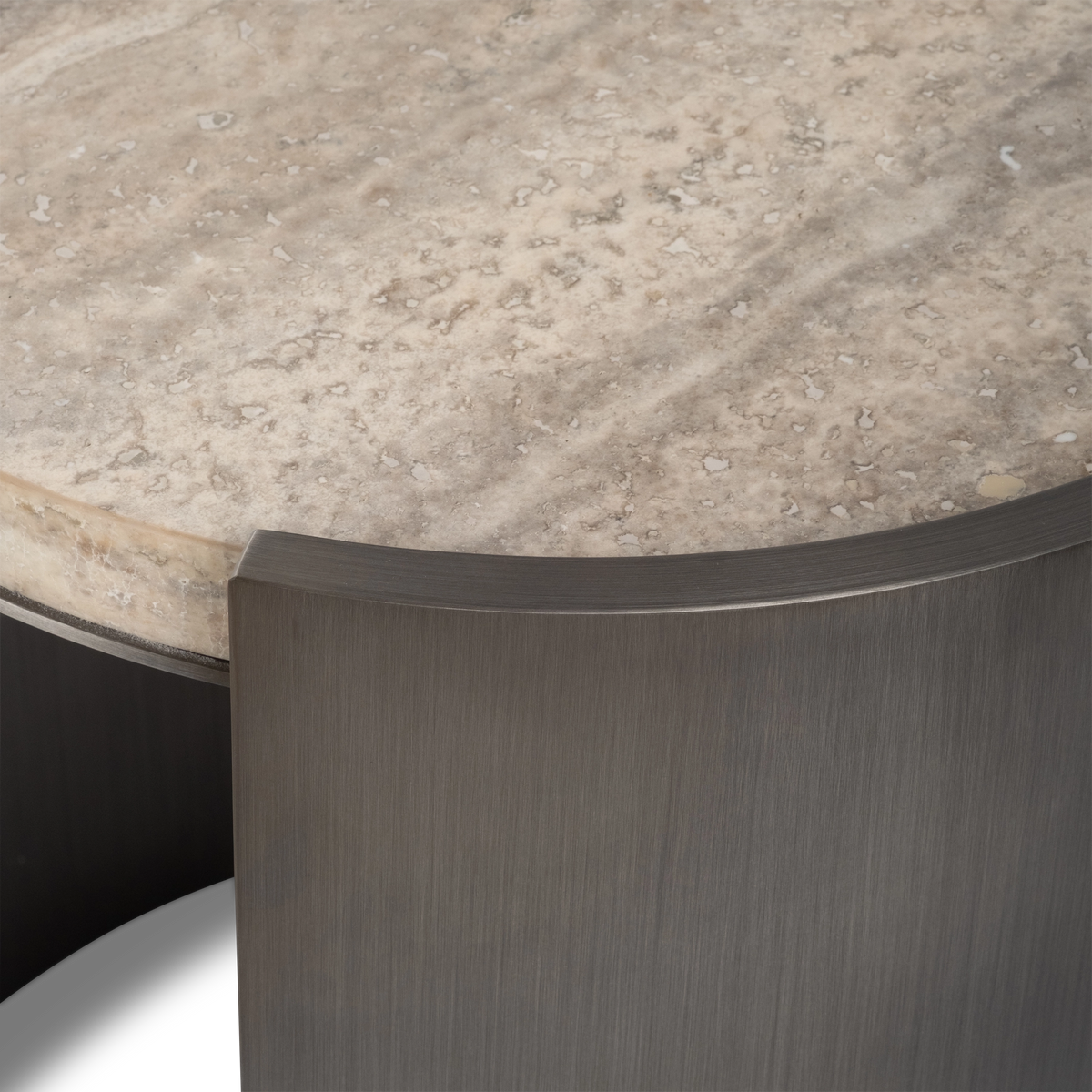 Close-up showing the Beam Side Table's taupe travertine edge with pale cream banding, resting beside a curved aged pewter metal panel with a crisp, squared top edge.