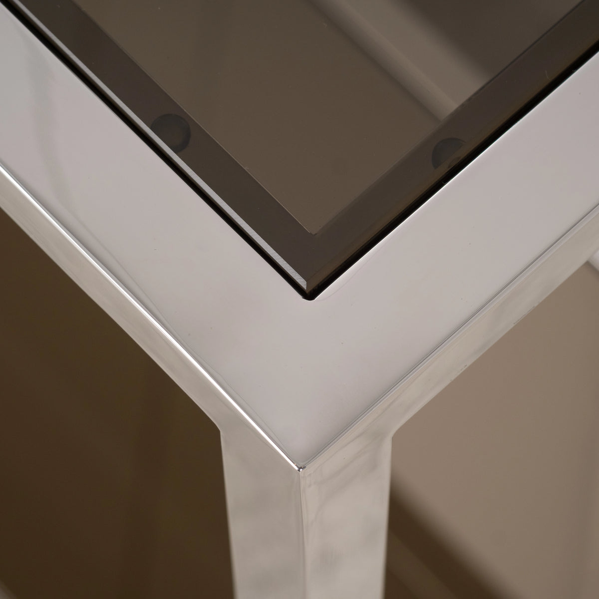 Close-up showing the corner of the Sandro Console Table in Polished Steel, with the mirror-bright frame, the beveled smoked glass edge, and small round glass pads along the rim.