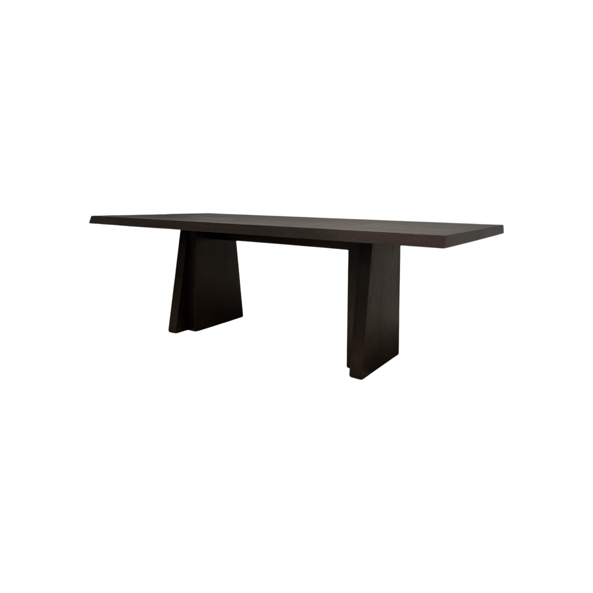Angled view of the Oblique 120-inch Dining Table showing its elongated dark wood top, chamfered edges and sculptural splayed pedestal bases.