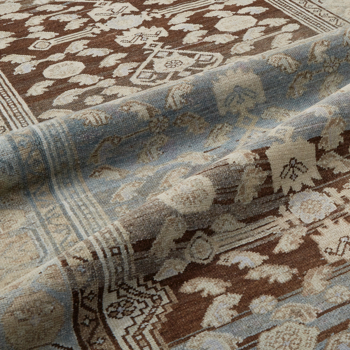A close-up of a patterned area rug with a brown and beige floral field and a light blue border with cream detailing.