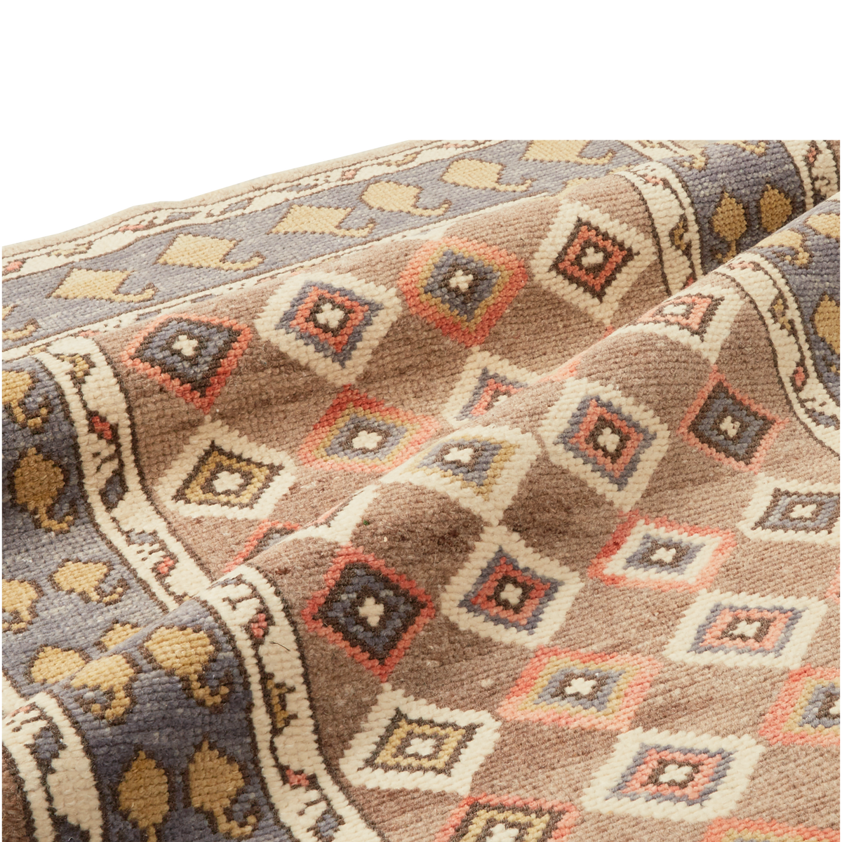 A close-up of a woven textile or rug with a geometric diamond pattern in beige, brown, gray, white, and muted coral tones, draped to show texture and pattern detail.