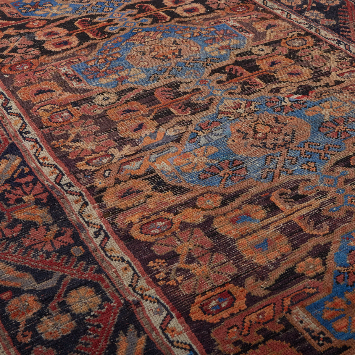 A close-up of an ornate traditional rug with a complex floral and geometric pattern in dark brown, rust red, light blue, beige, and black.