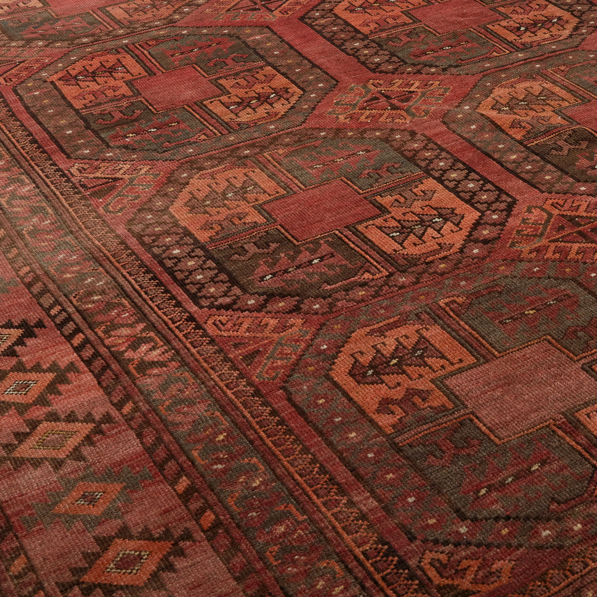 A close-up of a traditional patterned rug with geometric and tribal motifs in rust red, terracotta, olive green, and brown.
