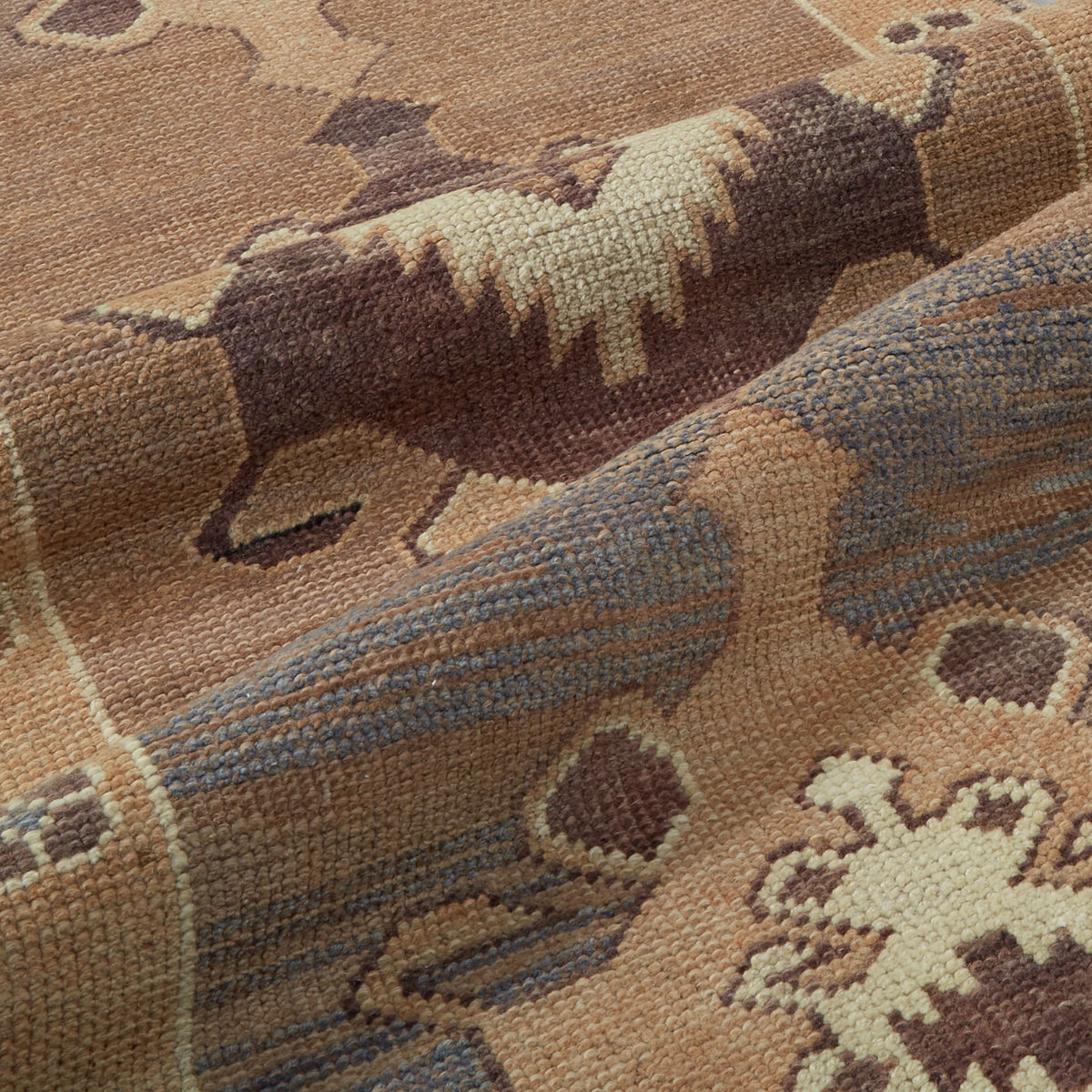 Close-up of a woven rug with a Southwestern-style animal and geometric pattern in tan, brown, cream, and muted blue-gray.